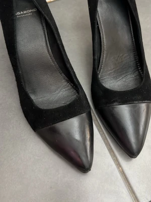 Svarta pumps från Vagabond - Säljer ett par klassiska svarta pumps från Vagabond med spetsig tå och låg klack. Skorna är i en mix av mocka och skinn, vilket ger en snygg kontrast mellan material och finish. Perfekta för dig som gillar stilrena och tidlösa skor.