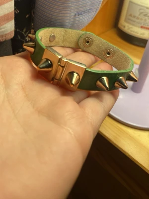 Valentino liknade Grönt nitar armband med spikes - Coolt grönt armband med silvriga spikes och tryckknappar. Armbandet har en bred läderrem och metallspänne framtill. Perfekt accessoar för att ge din outfit edge.