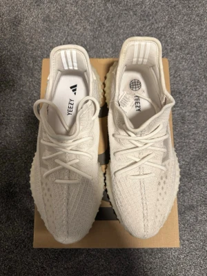 Adidas Yeezy Boost 350 V2 Cream White - Säljer ett par Adidas Yeezy Boost 350 V2 i färgen Cream White. Skorna har en stickad ovandel i vitt, klassisk ribbad sula och snörning. De är låga och har en chunky, bekväm sula som ger en modern vibe. Perfekta för dig som gillar streetwear och vill sticka ut.