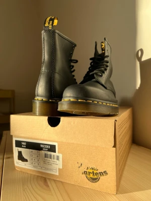 Ny EURO 41 - Dr. Martens 1460 boots - Säljer ett par klassiska svarta Dr. Martens 1460 boots med snörning och rund tå. Skorna har den ikoniska gula sömmen runt sulan och är tillverkade i skinn med en slitstark platt sula i syntet. Perfekt för dig som vill ha en tidlös och edgy stil.