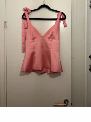 Rosa omlott linnetopp med rosett - Säljer en söt rosa linnetopp med omlott-design och knytband på axlarna som bildar fina rosetter. Toppen har en v-ringad hals och är lätt utsvängd nedtill. Perfekt för varma dagar och sommarhäng. Är i storlek xs men skulle säga den sitter som en s