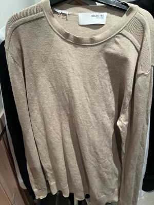 Beige stickad tröja från Selected Homme - Snygg beige stickad tröja från Selected Homme med rund hals och ribbade detaljer vid axlar och muddar. Perfekt för lager-på-lager och passar till jeans eller chinos. Långärmad och i mjukt material som känns skönt mot huden.