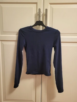 Marinblå långärmad topp med rund hals - Säljer en stilren marinblå långärmad topp med rund halsringning. Toppen har en slim passform och är tillverkad i mjukt material som sitter skönt mot kroppen. Perfekt att matcha med jeans eller kjol för en enkel och snygg look.