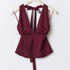 Vinröd halterneck topp - Snygg vinröd halterneck topp i satin med djup v-ringning och öppen rygg. Perfekt för festliga tillfällen! Den har knytband i nacken och midjan. Aldrig använd, med prislapp kvar. Nypris 359kr