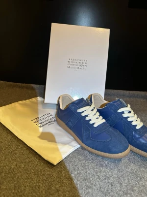 Blå Maison Margiela sneakers - Maison Margiela sneakers i blå mocka och skinn med vita snören och beige sula. Klassisk och stilren modell med rund tå och platt sula. Kommer med originalkartong och dustbag. Perfekta för dig som gillar exklusiva och trendiga sneakers. pris kan absolut diskuteras 