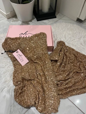 Glittrig guldklänning från Oh Polly - Oh polly klänning i storlek M. Den är stretchig  Glittrar extremt mycket och du sticker ut ganska mycket. ( glittrar extra i mörkret )  Slits på sidan av klänning alltså en öppning  Den är helt ny och kartongen kommer med  Den är använd endast en gång