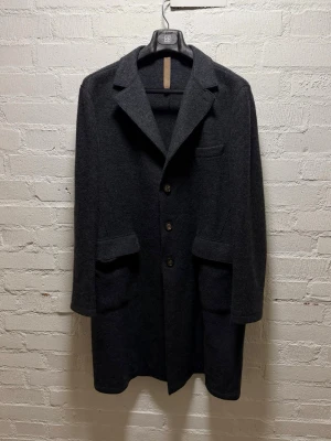 Eleventy Laser-cut Wool Coat - Snygg mörkgrå rock från Eleventy i mjuk ull. Klassisk design med tre knappar framtill, bred krage och stora fickor. Perfekt längd och stilren look som funkar till många outfits. Materialet är  ull och knapparna har Eleventy-logga. Storlek 56 (liten i storlek) Mått: Bröst: 61 cm Axlar: 49 cm Ärm: 67 cm Längd från axel: 99 cm  Knappt använd, nyskick!