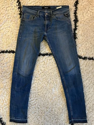 Replay jeans blå tapered 29/30 - Snygga blå jeans från Replay med klassisk femficksdesign och coola detaljer på bakfickorna. Modellen är tapered med smalare ben och slimfit passform. Materialet är slitstarkt jeans och färgen har en schysst tvättad look. Perfekt för dig som gillar stilrena och bekväma jeans.