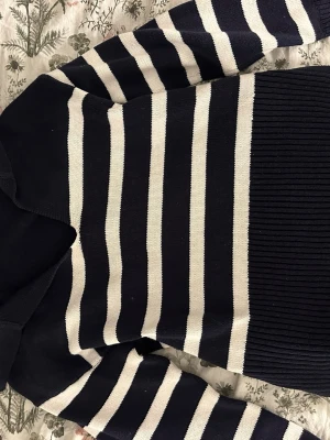 Marinblå och vit randig stickad tröja - Snygg stickad tröja med breda marinblå och vita ränder. Tröjan har långärmade ärmar och ribbad nederkant som ger en schysst passform. Perfekt för dig som gillar klassisk stil med en modern twist.