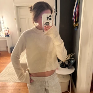 Beige stickad croppad tröja från COS - Supermjuk och croppad stickad tröja från COS i beige. Tröjan har lång ärm, rund halsringning och ribbade muddar. Perfekt att styla med jeans eller mjukisbyxor🩷