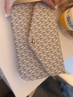 Vit och grå mikel kors - Snygg väska i färgen grå och  vitt. Insidan är klädd i rött tyg och väskan kommer med en matchande liten necessär med dragkedja . Perfekt för att hålla ordning på småsaker och ge din outfit en clean vibe. Har haft den endast i 5 månader. 