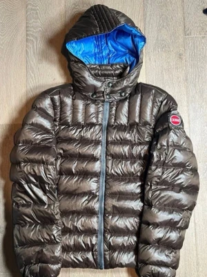 Colmar jacka - Snygg brun pufferjacka från Colmar med blått foder i huvan. Jackan har quiltad design, dragkedja framtill och långärmade armar. Perfekt för kalla dagar och har en modern look med logotyp på ärmen.