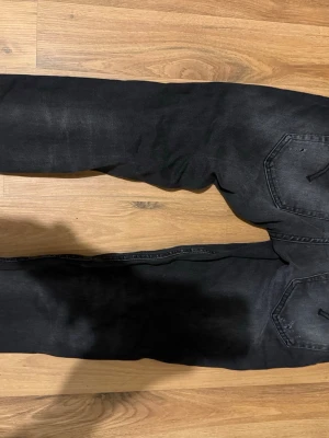 Dondup - Säljer ett par svarta jeans med coola slitningar och lätt tvättad look. Byxorna har klassiska fem fickor och bälteshällor. Materialet är jeans och passformen är rak med något smalare ben. Perfekt för dig som gillar en lite ruffare stil.