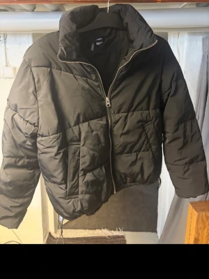 Svart pufferjacka från H&M Divided - Svart pufferjacka från H&M Divided i storlek S. Jackan har hög krage, dragkedja framtill och två sidofickor. Den är quiltad och har en loose passform som ger en chill vibe. Perfekt för kalla dagar när du vill vara både varm och snygg.