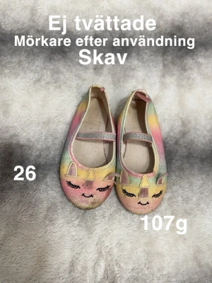 Färgglada ballerinaskor med enhörningsmotiv - Säljer ett par ballerinaskor i regnbågsfärger med glittrigt tyg och sött enhörningsansikte framtill. Skorna har elastiskt band över foten och platt sula. Perfekt för dig som gillar fantasifulla detaljer och mjuka pastelltoner.🌸Ej tvättade. Mörkare efter användning. skav. Har suttit lappar bakom skon.