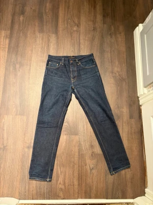 Mörkblå Nudie Jeans, storlek 30/30 - Säljer ett par mörkblå jeans från Nudie Jeans i storlek 30/30. Klassisk femficksmodell med orangea sömmar och Nudie-logga på bakfickorna. 
