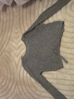 Grå croppad stickad tröja Hollister - Säljer en grå croppad stickad tröja från Hollister i storlek XS. Tröjan har långa ärmar och snygg snörning i ryggen som ger en extra detalj. Perfekt till höst och vinter för en chill och trendig look.