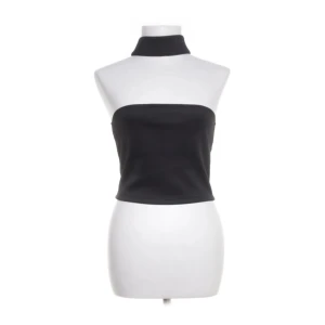 Svart topp med halterneck liknande design - Superfin svart topp med halterneck-design och bar axel framtill. Minimalistisk men samtidigt edgy – perfekt för både fest och vardag. Sitter snyggt och framhäver axlar och rygg tack vare den öppna racerback-liknande ryggen. Enkel att styla med jeans, kostymbyxor eller kjol.