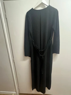 Svart långklänning med snörning - Säljer en svart långklänning med diagonalt ribbat mönster och långa ärmar. Klänningen har snörning i midjan för att justera passformen och en enkel rund halsringning. Materialet känns mjukt och har en lätt stretch på grund av ribbningen. Den är väldigt elegant och stilren och kan passa perfekt till både vardagen eller något finare event. Pris går alltid att diskuteras💕