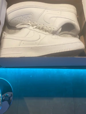 Nike Air Force 1 helvita sneakers - Säljer ett par klassiska Nike Air Force 1 sneakers i helvitt skinn. Modellen har rund tå, platt sula och snörning med metallplatta framtill. Ikonisk design med perforerade detaljer på tån och Nike-logga på sidan. Perfekt för dig som gillar cleana och tidlösa sneakers . Pris kan diskuteras vid snabbaffär