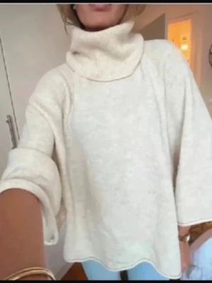 Beige polotröja med vida ärmar - Mysig beige polotröja med oversized passform och vida trekvartsärmar. Tröjan är stickad och har en hög, bred polokrage som ger en avslappnad och trendig look. Perfekt för lager på lager under höst och vinter.