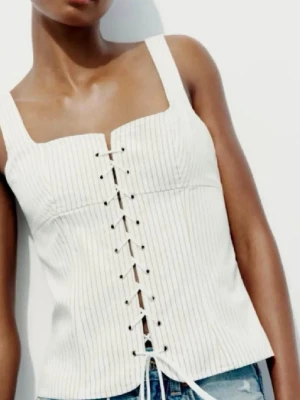 Vit randig korsettopp med snörning - Storleken är M men jag tycker den är typ samma som s! Säljer en vit korsettopp från Zara med tunna svarta ränder och snygg snörning framtill. Toppen har breda axelband och croppad passform som ger en modern siluett. Perfekt till jeans eller kjol för en trendig look.