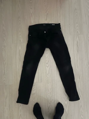 Svarta Replay Anbass jeans - Säljer ett par svarta Replay Anbass jeans i slim fit. Klassisk femficksmodell med smal passform och snyggt snitt. Jeansen är tillverkade i stretchigt material för extra komfort och har diskreta detaljer. Perfekta för dig som gillar stilrena och moderna jeans.