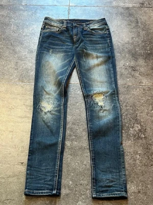 Blå jeans från Nudie med slitningar - Säljer ett par otrolig snygga vintage Nudie jeans i storleken 28/33 men jag skulle säga att de sitter mer som 28/32, de har en gaaalen wash och as schyssta slitingar, pris går att diskutera, jag skulle även kunna tänka mig att göra ett byte, så kom med prisförslag och byten, mvh💪💯
