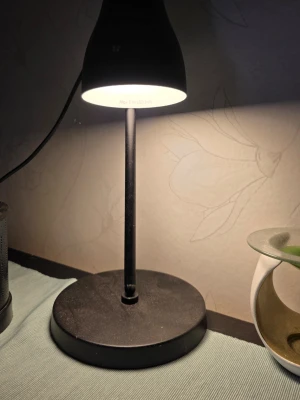 Lampa svart bordslampa  - Bilderna visar en svart bordslampa med rund fot och smal stång. 