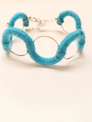 Turkos vågig armbandsdesign - Unikt armband med vågig form, tillverkat av silverfärgad metall och inslaget med turkost garn. Lätt och bekvämt med justerbart lås, perfekt för att ge din stil en färgklick. Passar dig som gillar kreativa och handgjorda accessoarer.