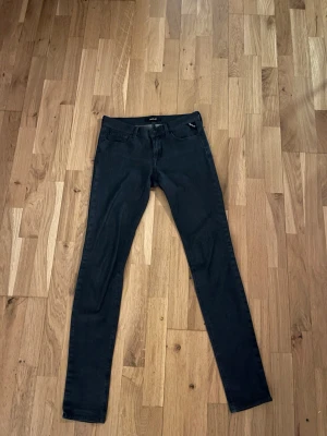 Marinblå slim  jeans från Replay - Säljer ett par svarta skinny jeans från Replay med klassisk femficksdesign och smal passform. Jeansen har en mörk ton och är tillverkade i stretchigt jeansmaterial för extra komfort. Perfekt för dig som gillar en tajt siluett och stilren look.