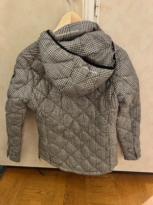 Rutig quiltad pufferjacka Canada Snow - Säljer en sjukt snygg pufferjacka från Canada Snow med rutigt mönster i svart och vitt. Gulddetaljerna gör mycket med hela jackan! 