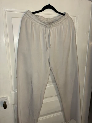 Vita mjukisbyxor med snörning - Säljer ett par vita mjukisbyxor med elastisk midja och snörning från Lager 157. Byxorna har en loose passform och är tillverkade i mjukt bomullsmaterial. Perfekta för chill dagar eller när du vill vara extra bekväm.