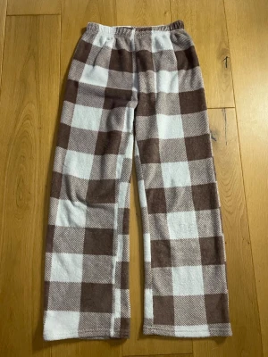 Gammel rosa och vita rutiga mjukisbyxor - Supermysiga mjukisbyxor med stora bruna och vita rutor. Byxorna har resår i midjan och är raka i modellen, perfekta för chill dagar hemma. Materialet är mjukt och fleece-liknande för extra komfort.