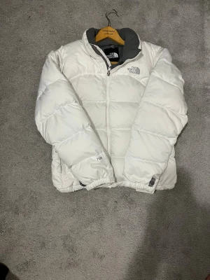 Vit pufferjacka från The North Face - Säljer en riktigt fet vit pufferjacka från The North Face, modell 700. Jackan har hög krage, dragkedja framtill och grått innerfoder. Perfekt för kalla dagar och har en clean, oversized look. Logga på bröstet och ryggen. Passar dig som vill ha både stil och värme.