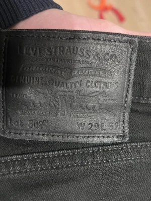 Levi's 502 svarta jeans W29 L32 - Säljer ett par svarta Levi's 502 jeans med klassisk femficksdesign och raka ben. Jeansen har en snygg svart läderpatch bak i midjan och diskret röd Levi's-tagg på bakfickan. Tillverkade i mjukt och slitstarkt denimtyg som sitter riktigt bra.