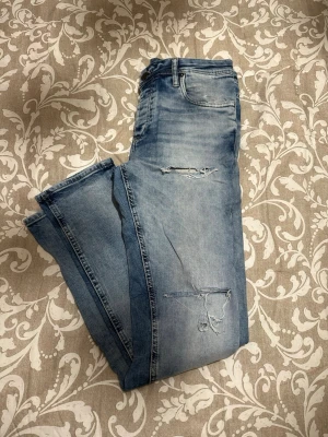 Slim fit jeans Tim med slitningar - Snygga ljusblå slim fit jeans från Tim med slitna detaljer på låren och knäna. Klassisk femficksmodell med knapp och dragkedja i midjan. Jeansen har en smal passform och är tillverkade i mjukt denimtyg som ger en skön känsla.