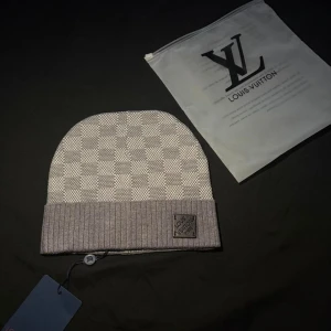 grå-rutig mössa - Snygg mössa  grått med klassiskt rutmönster och ribbad uppvikt kant. Märkets logopatch sitter framtill på kanten. Perfekt accessoar för dig som gillar exklusiv streetstyle och vill sticka ut med designerplagg.