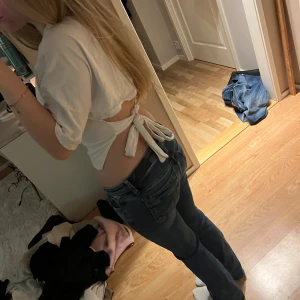 Vit croppad topp med knyt i ryggen - Säljer en vit croppad topp med korta ärmar och snygg knytning i ryggen. Toppen har en enkel och clean look framtill och öppen rygg som ger en cool vibe. Perfekt till jeans eller kjol för en trendig outfit.