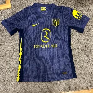 Atlético Madrid Griezmann Nike fotbollströja - Säljer en officiell helt nyAtlético Madrid bortatröja från Nike med Griezmann och nummer 7 på ryggen med etikett. Tröjan är marinblå med gula detaljer, klubbmärke och sponsortryck. Tillverkad i lätt och ventilerande Dri-FIT-material, perfekt för match eller träning. Skriv vid minsta fundering. Priset kan diskuteras!