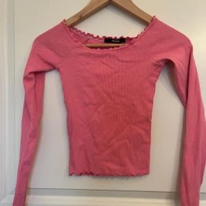 Rosa ribbad topp från BikBok XS - Supersöt rosa långärmad topp från BikBok i ribbad bomull. Toppen har volangdetaljer vid halsringning och nederkant som ger en gullig touch. Perfekt att styla med jeans eller kjol för en fräsch look.