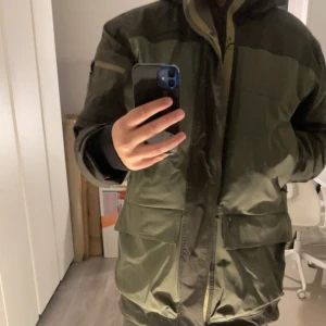 Grön parkajacka Peak Performance M - Säljer en grön parkajacka från Peak Performance, modell 2L Stretch Parka FW23. Jackan har huva, stora fickor framtill och dragkedja. Materialet är syntet med stretch och jackan har en loose passform. Perfekt för dig som gillar stilren och funktionell design. Jackan är bara använd under en 3dagars period i Bad Gastein och säljer då jag söker något annat, nypris ligger på 8-tusen!