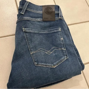 Replay Anbass L30 - Snygga Replay Anbass jeans i klassisk blå tvätt med lätt slitning. Bekväm modell i nyskick. Använda knappt 1 gång. W30 L29 Nypris:1699kr