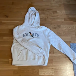 Hoodie från Axel Arigato - Säljer en stilren beige hoodie från Axel Arigato med en färgglad fågelbroderi och text på bröstet. Storlek S. Använd endast ett fåtal gånger. 