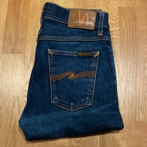 Nudie Jeans blå - Snygga blå jeans från Nudie Jeans i modellen Shorty Red. Jeansen har klassiska orange sömmar, fem fickor och är tillverkade av 98% ekologisk bomull och 2% elastan för extra stretch. Perfekt passform och coola slitningar på benen. Pris kan diskuteras vid snabb affär!