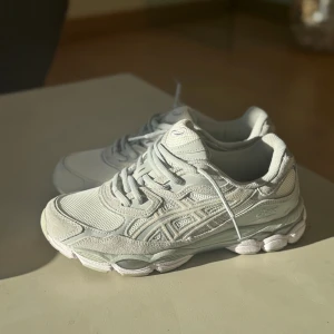 Vita Asics sneakers med mesh och mocka - Snygga vita Asics cloud/grey sneakers med detaljer i mesh. Skorna har snörning och en chunky, mönstrad sula som ger grym komfort. Perfekt för dig som gillar stilrena och sportiga sneakers med modern vibe. Aldrig använda