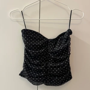 Svart prickig tubtopp - Säljer en svart tubtopp med vita prickar. Toppen har rynkade detaljer framtill och är figurnära. Perfekt för dig som gillar en söt och trendig look💋