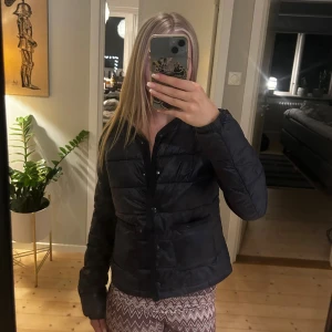 Mörkblå pufferjacka från Gina Tricot - Säljer en svart pufferjacka från Gina Tricot i storlek 158/164. Jackan har en stilren look med knappar framtill, två fickor och långärmade armar. Perfekt för dig som vill ha en enkel och snygg jacka till höst och vinter.