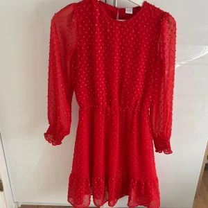 Röd prickig klänning från Lindex barn - Superfin röd klänning från Lindex med transparenta långärmar och små prickar i tyget. Klänningen har resår i midjan, volang nertill och knäppning bak i nacken. Perfekt för dig som vill sticka ut med en färgstark look!