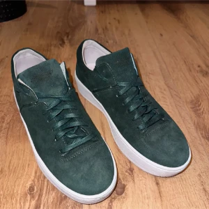 Mörkgröna mocka skor från Jim Ricky - Snygga mörkgröna sneakers från Jim Rickymed ovandel i mocka och vita platta sulor. Skorna har rund tå, snörning och stilren design som passar till jeans eller shorts. Väldigt fint skick och säljs endast för 299 kronor storlek 40